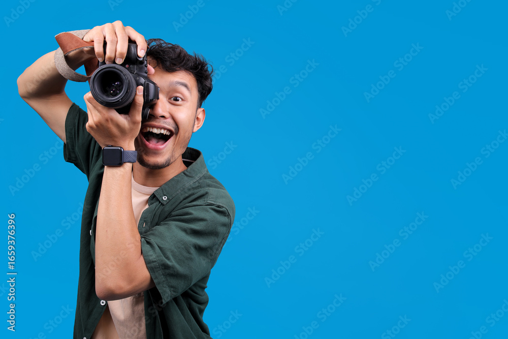 Obraz premium Excited Male Photographer Holds A Camera, Taking A Picture With Smiling, Isolated On Blue Background