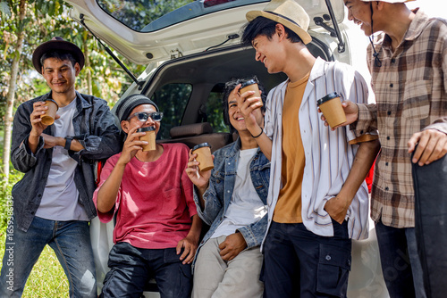 Five Friends Drink Coffee And Relax By The Open Trunk Of A Car On A Sunny Day During Their Road Trip