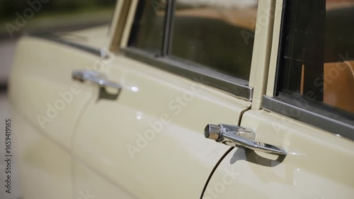 Chrome door handle with button of old vintage beige car on sunny day close up. Exterior of retro sedan from 80s in parking lot during journey.