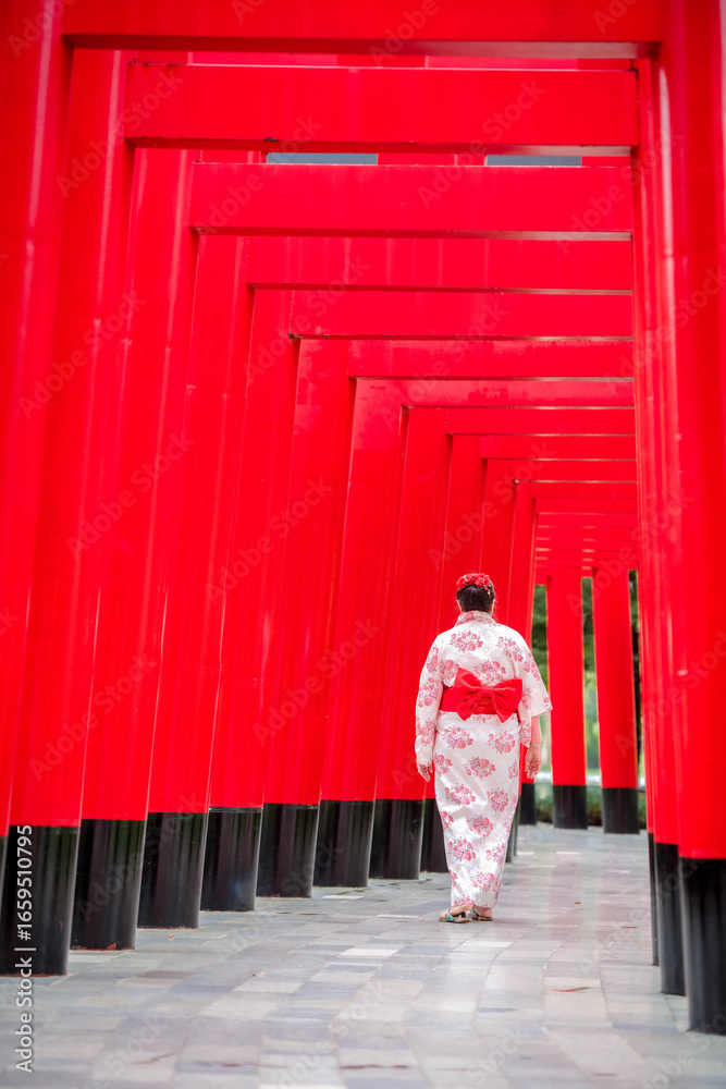 Fototapeta premium elderly Asian woman wearing a traditional Japanese yukata walks along a path with torii gates at a Japanese temple in Thailand.
