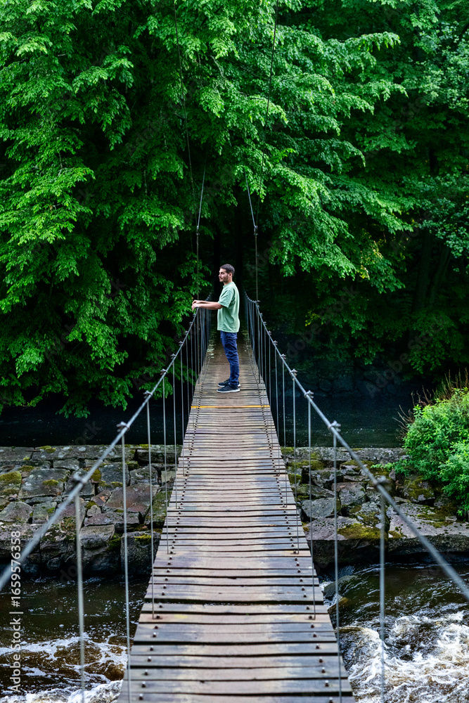 Fototapeta premium Mann steht auf Hängebrücke über Fluss Mörrumsån mitten im Wald in Blekinge Schweden