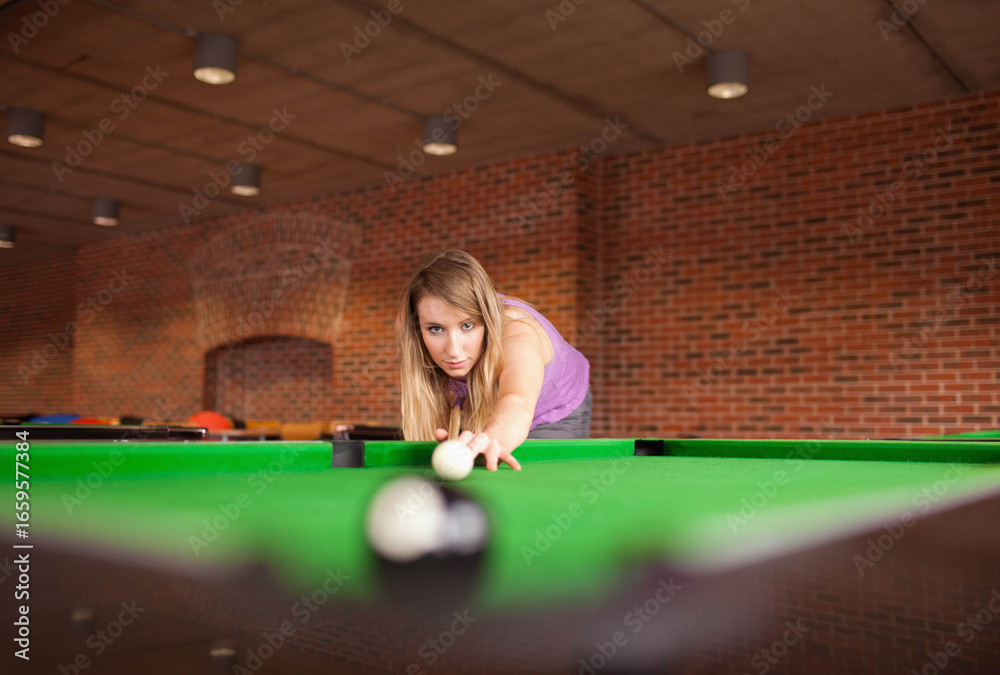 Naklejka premium Woman in purple sportswear playing billiards in recreation room lining up shot on green-felt table