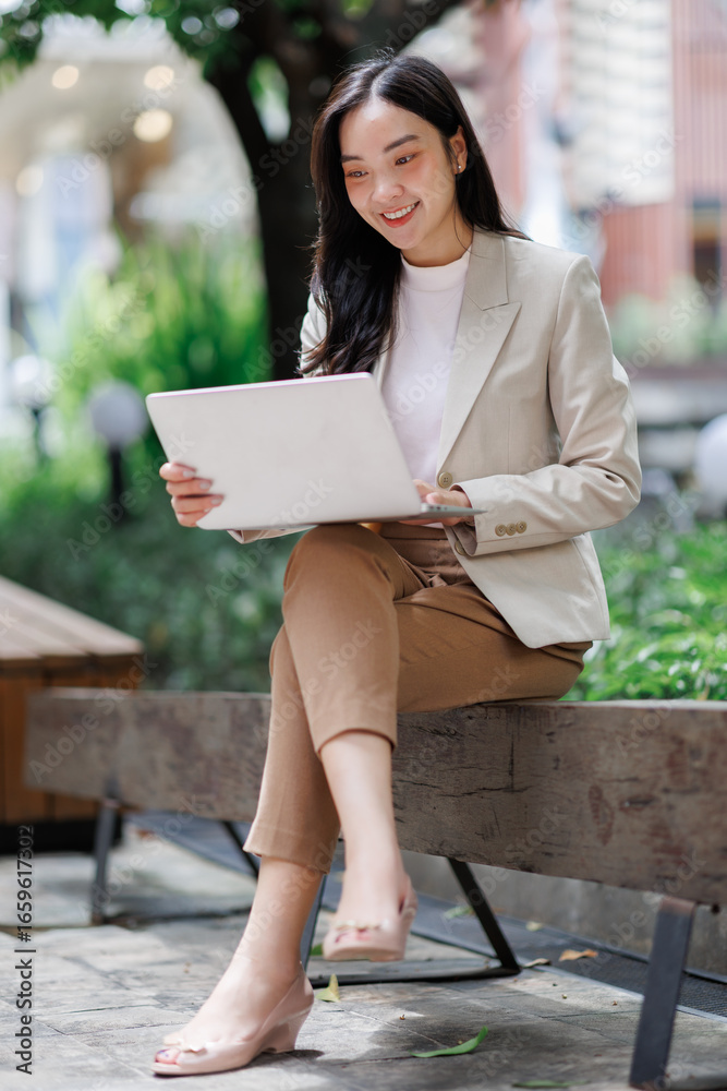 Obraz premium Smiling businesswoman working on laptop outdoors in urban setting