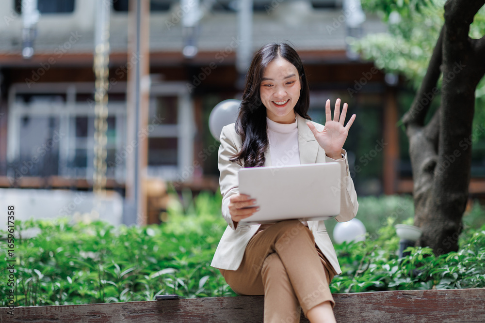 Fototapeta premium Asian businesswoman video calling and waving outdoors