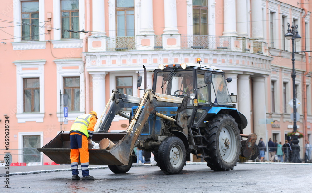 Fototapeta premium A road worker stands next to a tractor in the middle of a newly paved road, Nevsky Prospekt, Saint Petersburg, Russia, August 18, 2025
