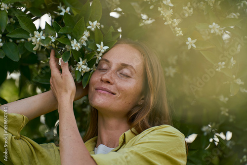 Woman with eyes closed near orange blossom flower in garden