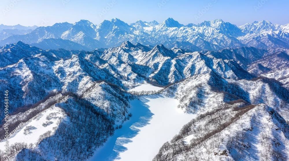 Obraz premium Snow-covered mountains and valleys stretch across the landscape, showcasing a serene winter scene ideal for travel articles, winter sports promotions, or nature-themed designs,