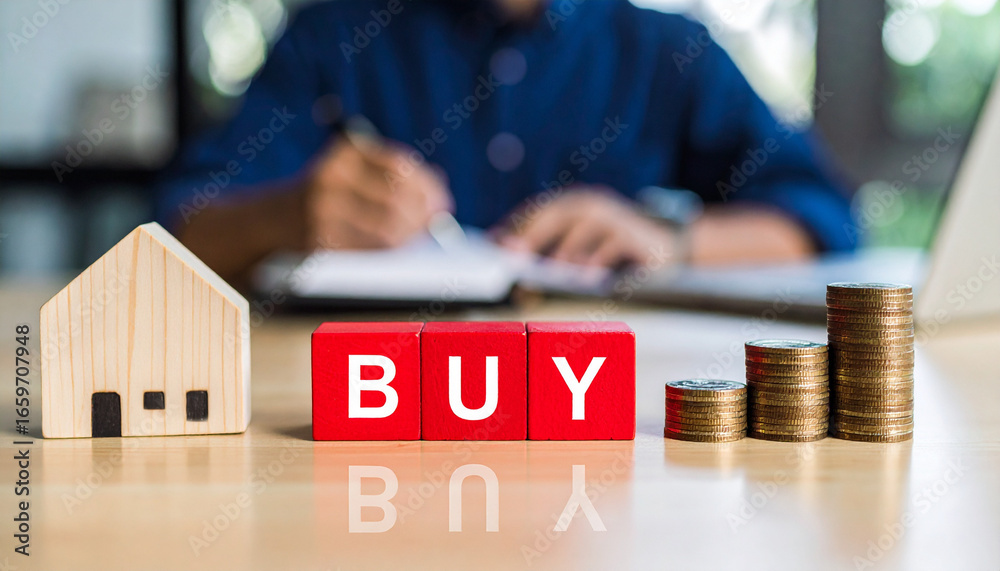 Fototapeta premium Real estate concept featuring a small wooden house, the word BUY in block letters, and stacks of coins with a person in the background. The image conveys themes of property investment.