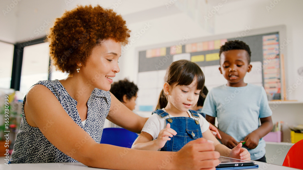 Fototapeta premium Female Teacher With Multi-Cultural Elementary School Pupils Using Digital Tablets At School