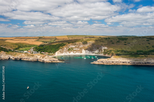 Wallpaper Mural Aerial view of turquoise waters meeting chalky cliffs and verdant hills under a bright, cloud-strewn sky at Lulworth Cove, Wareham, England, United Kingdom. Torontodigital.ca