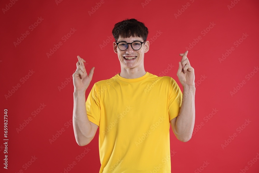 Naklejka premium Happy student crossing fingers for good exam result on red background