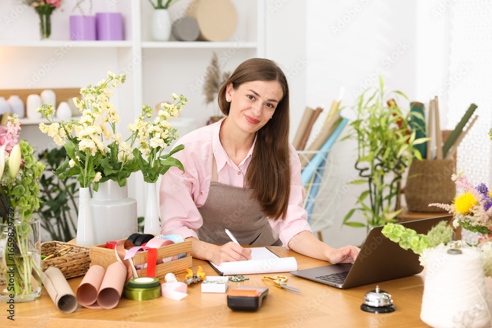 Professional florist working with laptop at wooden table in shop Professional florist working with laptop at wooden table in shop