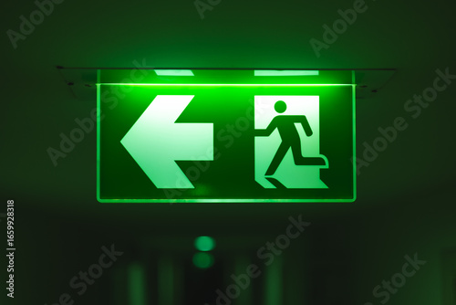 Exit way arrow direction guidance sign green color light emergency exit sign in a dark room