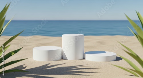 Three white cylindrical display stands situated on a sandy beach with calm blue ocean water in the background framed by green tropical leaves summer empty