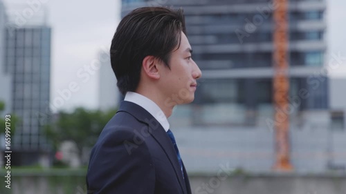 ビルを背景に遠くを見つめるスーツを着た日本人ビジネスマンの男性	