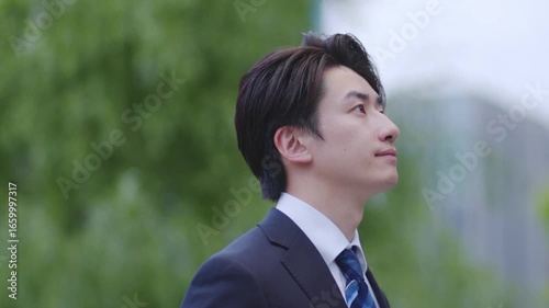 ビルを背景に遠くを見つめるスーツを着た日本人ビジネスマンの男性	