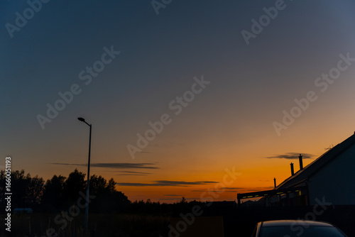 Foto Dramatic sunset sky with orange and blue gradient over suburban residential area with street lamp and house silhouettes