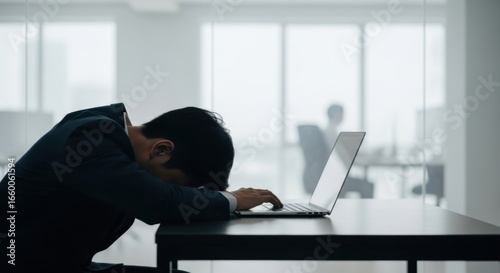Young Man Wearing Dark Suit Stressed Resting Head on Desk in Modern Office