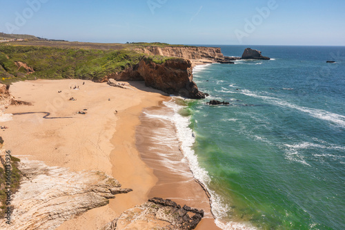 Panther Beach in Cotoni-Coast Dairies State Beaches, California. Aerial view of golden sand, dramatic cliffs, turquoise waves, and scenic shoreline near Highway 1 under a bright blue sky
