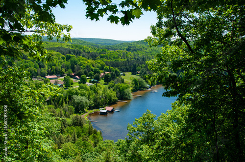 A breathtaking aerial shot captures a serene lake surrounded by lush greenery and scatterings of cozy houses, in a picturesque countryside during the summer season.