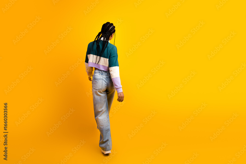 Naklejka premium Stylish young woman in casual attire walking against a vibrant yellow background showcasing modern fashion and confidence