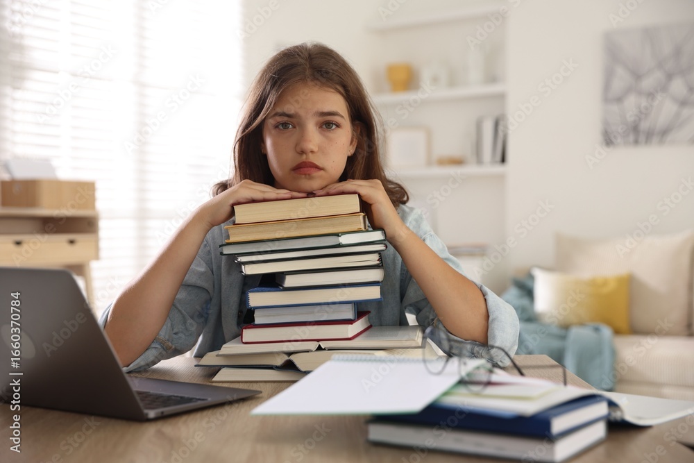 Tired student with stack of books preparing for exam at table indoors Tired student with stack of books preparing for exam at table indoors