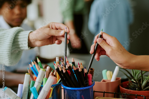 Foto Caucasian child and Black child reaching for colored pencils from container, han