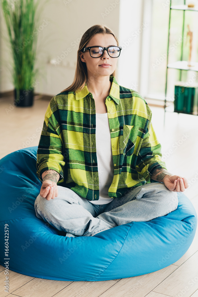 Obraz premium Young woman meditating on bean bag in casual interior, exhibiting mindfulness while balancing professional and leisure pursuits
