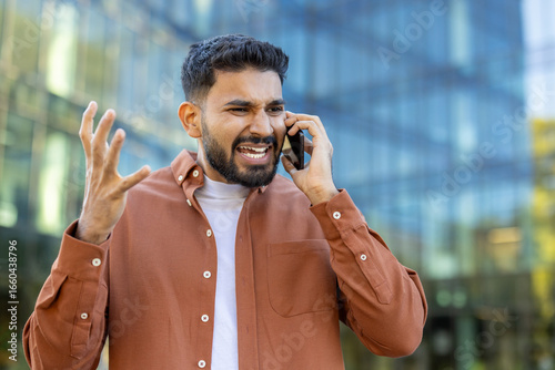 Photography Frustrated man on phone with modern building background, expressing annoyance