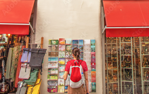 Tourist choosing postcards at a street shop with souvenirs and colorful displays.