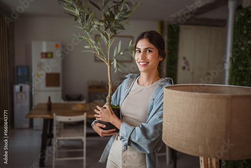 Fotografi Woman decorating living room holding potted plant