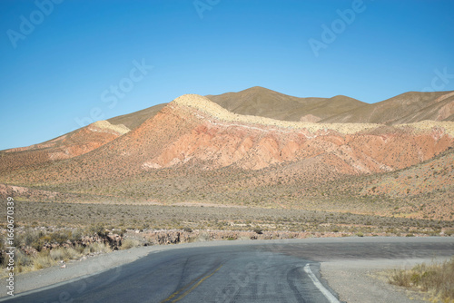 Empty desert highway stretches into hazy mountains under a clear sky