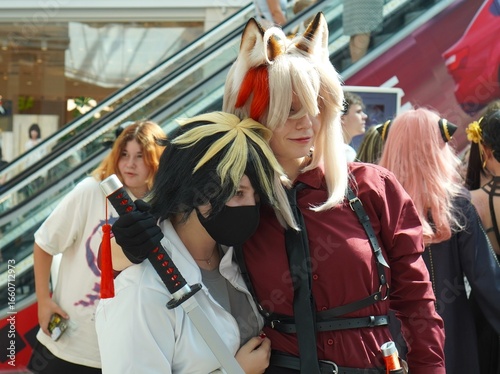 Two people dressed in anime costumes embrace each other at a celebration. They demonstrate their friendly relationship amidst the bustling event,