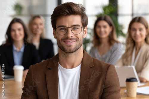 Handsome, confident, business professional wearing glasses, smiles directly, surrounded coworkers. Group workplace setting, successful leadership concept. Teamwork, cooperation, office,