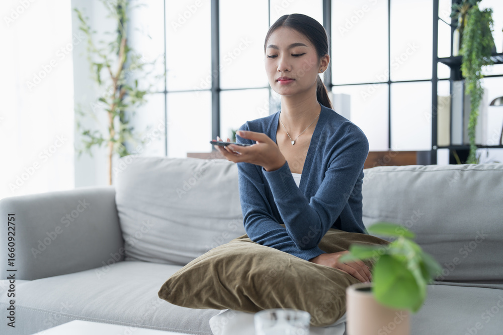 Asian woman Watching smart TV and using remote controller Hand holding television audio remote control at home with the remote control television Asian woman Watching smart TV and using remote controller Hand holding television audio remote control at home with the remote control television