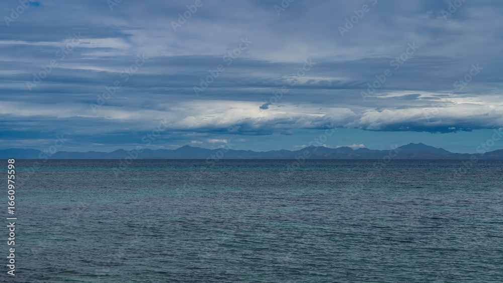 Obraz premium Calm minimalistic seascape. Ripples on the surface of the turquoise ocean. Mountains on the horizon. Blue sky, clouds. Madagascar.
