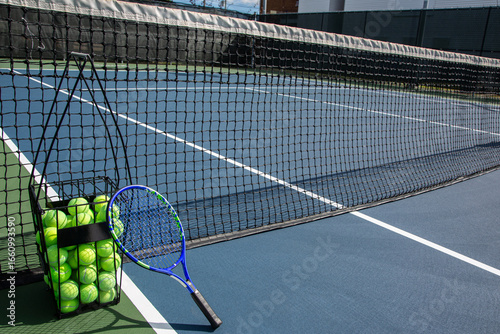 Panier de balles de tennis et raquette contre le filet
