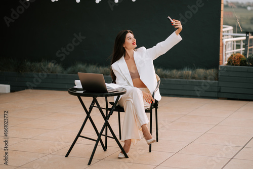 Professional woman enjoying a selfie while working on a rooftop terrace in the evening