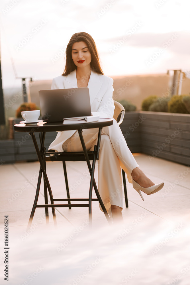 Fototapeta premium Young professional working outdoors at sunset while enjoying coffee