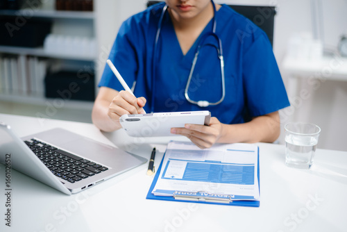 Doctor or nurse working on laptop to manage digital health records and patient information. Real people in medical office