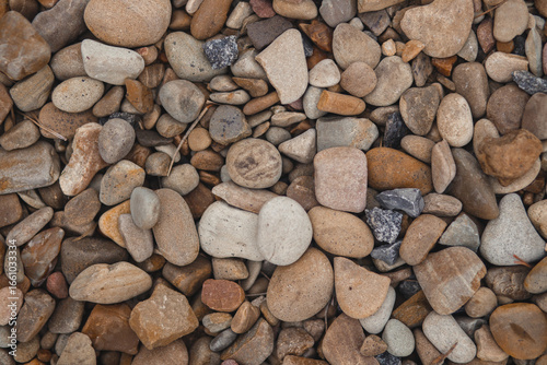 A top-down, detailed texture of smooth, multi-colored river stones and pebbles, creating a natural and abstract background.