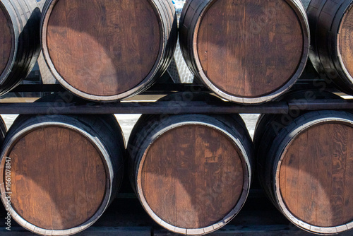Oak barrels stand in two rows to the horizon. Wooden barrels tied with steel hoops in the sun. Metal and natural wood of wine barrels, perspective view.