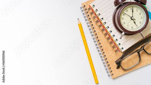Focused student studying with alarm clock, notebook, pencil, and glasses on white background