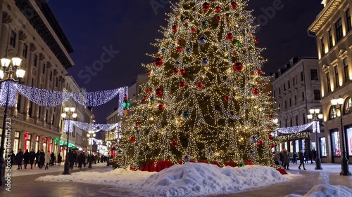 Festive city street at night with a towering Christmas tree, captured from a low angle. Perfect for a holiday-themed video backdrop.