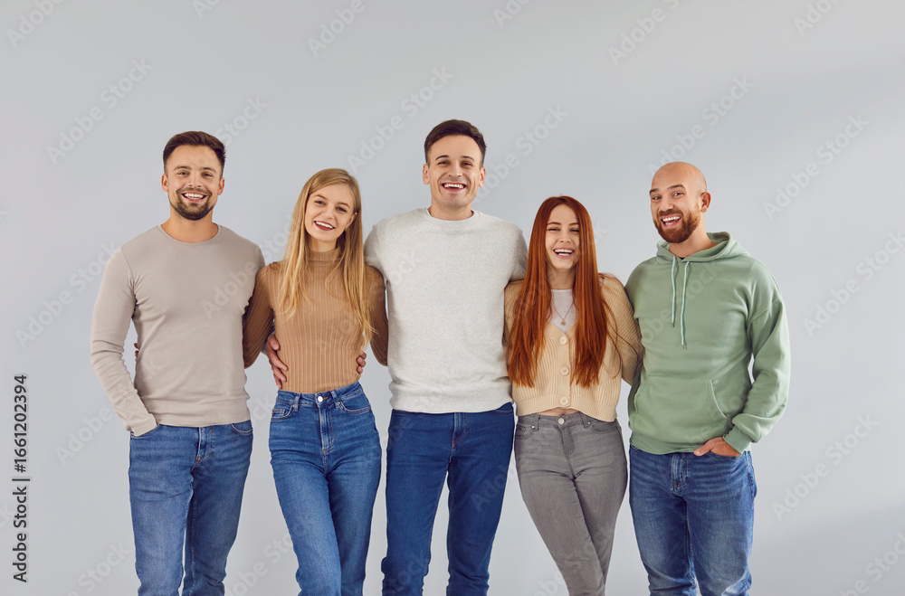 Obraz premium Indoor group portrait of 5 happy, joyful adult male and female friends. Five cheerful, smiling people wearing casual clothes standing together by a light gray wall