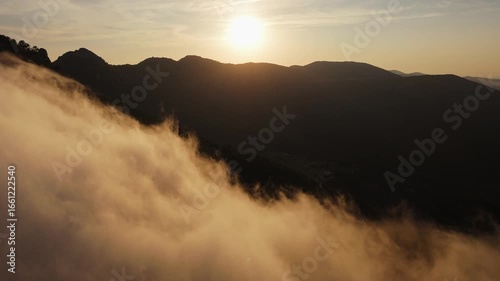 Drone video of mountain peaks surrounded by golden clouds at sunset, with warm light illuminating the misty slopes in Spain.