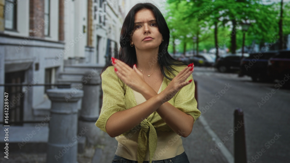 Fototapeta premium Hispanic woman standing with crossed arms on street outside classic building in daylight; rejection.