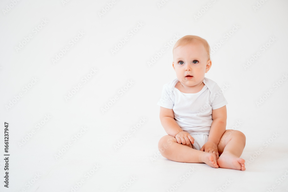 a baby in a white bodysuit on a white isolated background, space for text, a small child sitting on a white floor and smiling a baby in a white bodysuit on a white isolated background, space for text, a small child sitting on a white floor and smiling