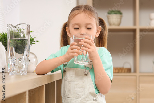 Cute little girl drinking water at home