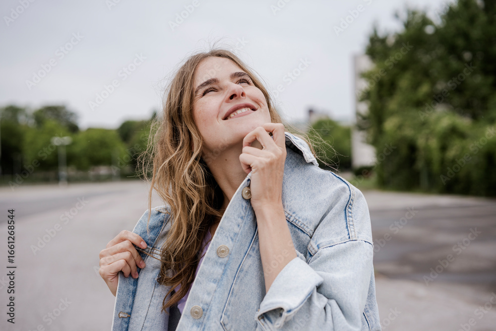 Smiling woman in denim jacket looking up outdoors in casual style Smiling woman in denim jacket looking up outdoors in casual style